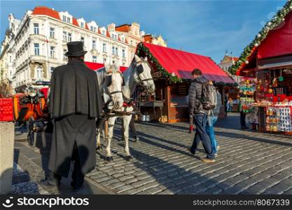 Coachman in a black hat and coat and white horses hitched to horse carriage waiting for tourists on Christmas Old Town Square of Prague, Czech Republic.