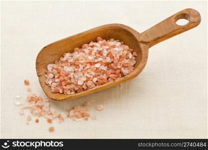 coarse crystals of pink and orange Himalayan salt on rustic wooden scoop