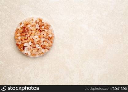 coarse pink Himalayan salt. coarse crystals of pink Himalayan salt in a round bowl against ceramic tile background, top view with a copy space