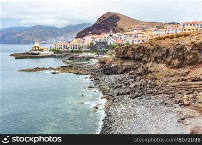 Coast in Madeira with sea stony beach mountains and village with houses