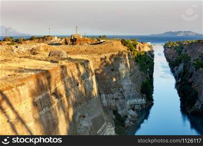 Coastal fortifications of the Corinth Canal in Greece in the bright rays of the rising sun and the horizon in the morning sea haze, image with copy space.. Coastal fortifications of the Corinth Canal in Greece in the bright rays of the morning rising sun.