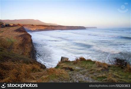Coastal landscape at sunrise with cliffs and misty glow