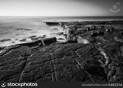 Coastal landscape at sunrise with cliffs and misty glow in black and white