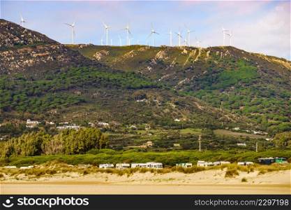 Coastal landscape. Many caravan vehicles camping on sea coast. Wind turbines oh hill. Mediterranean region of Costa del Sol, Spain.. Camper vehicles on beach, Spain