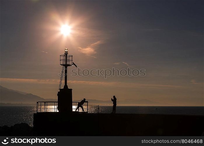 Coastal landscape with lighthouse in backlight in the morning with people in relaxation