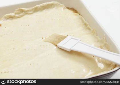 coating the surface of a meat pie with an egg and water mixture to prepare it for the oven