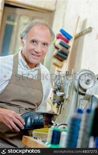 Cobbler holding shoe, stood next to sewing machine