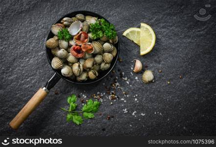 Cockles shellfish seafood plate with herbs and spices on dark background - blood cockle peeled on pan