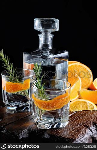 Cocktail classic Dry Gin with tonic and orange zest with a sprig of rosemary on a wooden board with slices juicy orange