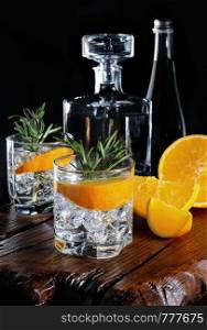 Cocktail classic Dry Gin with tonic and orange zest with a sprig of rosemary on a wooden board with slices juicy orange
