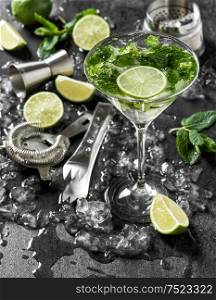 Cocktail drink with lime, mint and ice. Bar tolls and ingredients on dark background