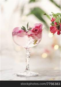 Cocktail in ch&agne glass with pink rose petal and green leaf at grey table with blurred background. Romantic fancy drink for celebration. Front view.