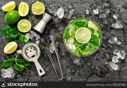 Cocktail juice with lime, mint and ice. Bar drink accessories on black table background. Alcoholic and nonalcoholic cold drinks. Selective focus