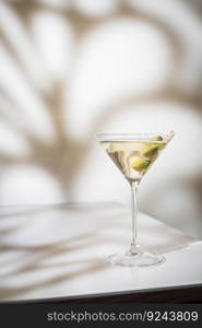 Cocktail vodka martini with green olives on light background with bright beautiful shadows. Cocktail vodka martini