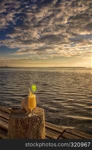 Cocktail with a straw on a wooden table. against the backdrop of the sea sunrise, ocean, at sunset. cocktail in vacation on a tropical island.