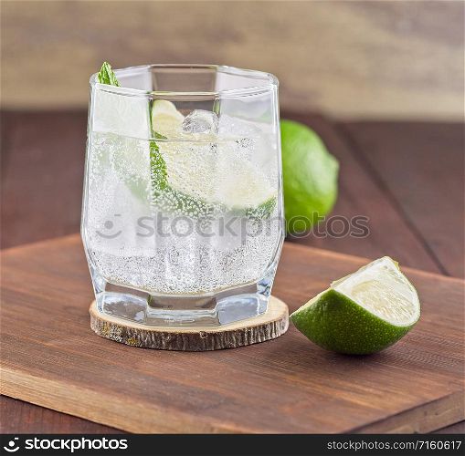 Cocktail with lime and mint leafs on wooden background. Fresh cocktail with lime, ice and mint