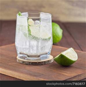 Cocktail with lime and mint leafs on wooden background. Fresh cocktail with lime, ice and mint