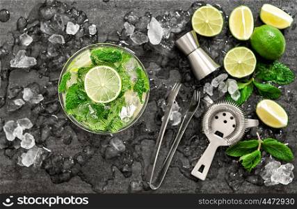 Cocktail with lime, mint and ice. Bar drink accessories on black table background. Alcoholic and nonalcoholic cold drinks. Selective focus