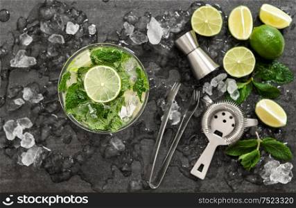 Cocktail with lime, mint and ice. Bar drink accessories on black table background. Top view. Selective focus