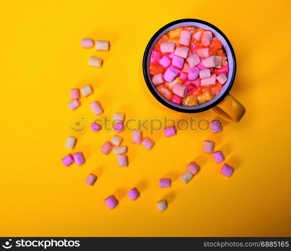 cocoa drink in a yellow mug with marshmallow slices on a yellow background, top view