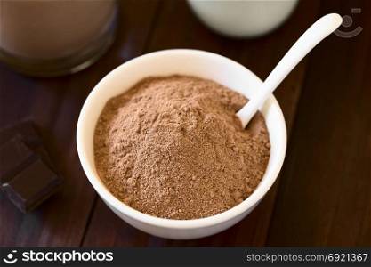 Cocoa or chocolate drink powder in bowl with spoon, chocolate drink and milk in the back, photographed with natural light (Selective Focus, Focus on the front of the cocoa). Cocoa or Chocolate Drink Powder