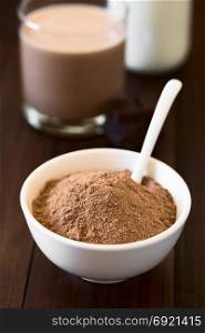 Cocoa or chocolate drink powder in bowl with spoon, chocolate drink and milk in the back, photographed with natural light (Selective Focus, Focus one third into the image). Cocoa or Chocolate Drink Powder