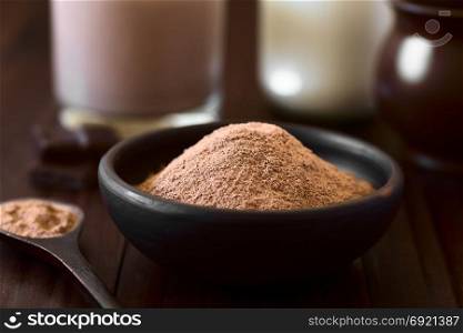 Cocoa or chocolate drink powder in rustic bowl, chocolate drink and milk in the back, photographed with natural light (Selective Focus, Focus one third into the cocoa). Cocoa or Chocolate Drink Powder