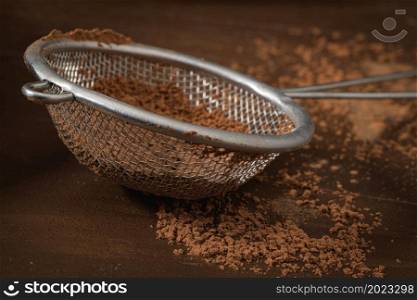 Cocoa powder in sifter on brown background.