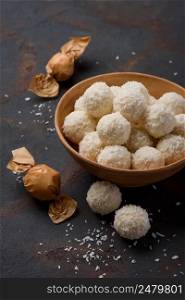 Coconut candies in bowl and wrapped on dark table background