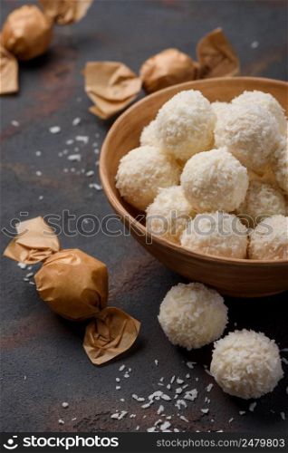 Coconut candy in bowl and wrapped in paper on dark table background