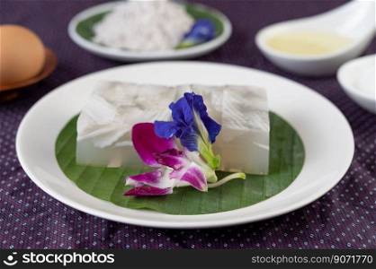 Coconut jelly is placed on a banana leaf in a white dish with butterfly pea flowers and with orchids.