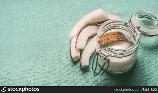Coconut milk in glass jar with coconut slices on turquoise background with copy space