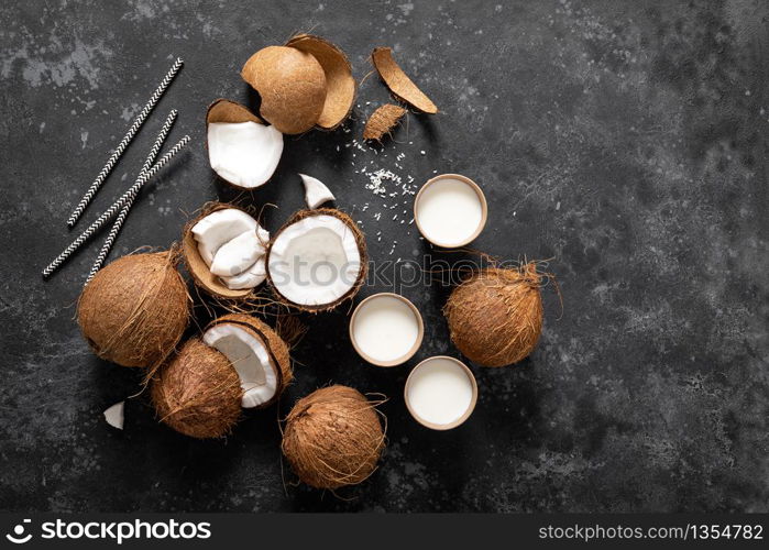 Coconut milk, whole and cracked coconuts on black background, top view