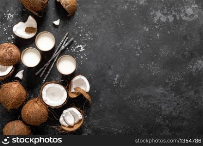 Coconut milk, whole and cracked coconuts on black background, top view