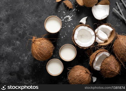 Coconut milk, whole and cracked coconuts on black background, top view