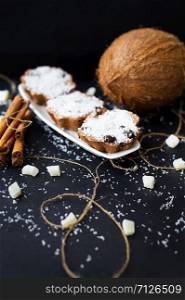 coconut muffins on a black background with cinnamon sticks and whole coconut slices and candied. coconut muffins on a black background
