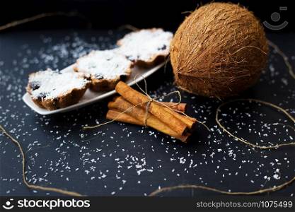 coconut muffins on a white plate with whole coconut and cinnamon sticks. coconut muffins on a black background
