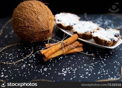 coconut muffins on a white plate with whole coconut and cinnamon sticks. coconut muffins on a black background