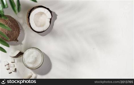 Coconut oil and coconuts on a white concrete background, the shadow he leaves of a palm tree on the table. Layout with copy space. Organic Coconut Oil for Spa and Health Care