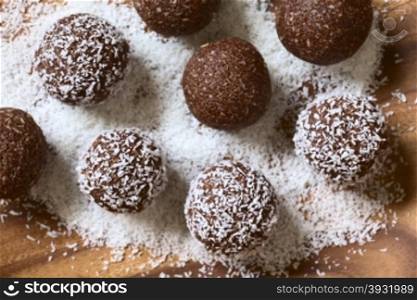 Coconut rum balls being covered with grated coconut on wooden plate, photographed overhead with natural light (Selective Focus, Focus on the top of the balls)