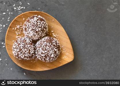 Coconut rum balls on small wooden plate, photographed overhead om slate with natural light (Selective Focus, Focus on the top of the balls)