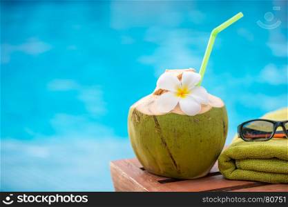 coconut with a straw on the edge of a deckchair against a blue water pool background