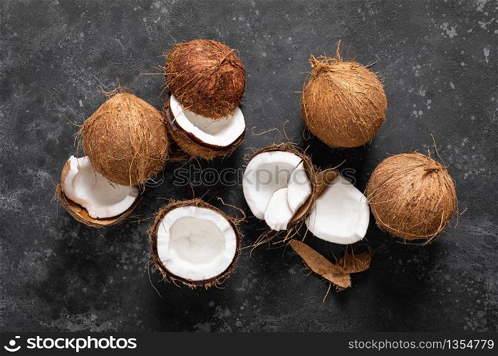 Coconuts cracked and whole on black background, top view