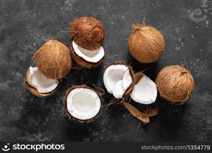 Coconuts cracked and whole on black background, top view