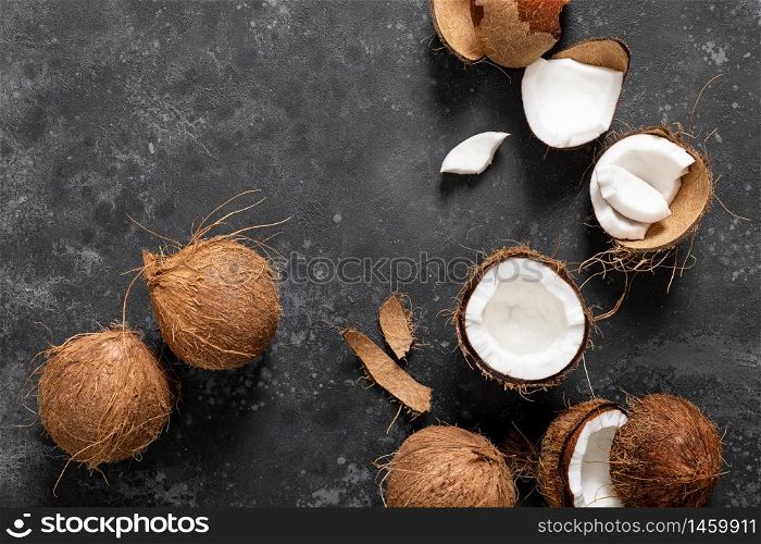 Coconuts cracked and whole on black background, top view