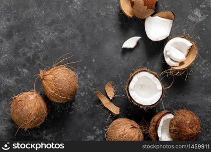 Coconuts cracked and whole on black background, top view