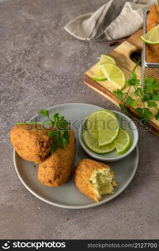 "Cod dumplings, or "bolinhos de bacalhau" and parsley leaves and lemons on wooden cutting board in a kitchen counter top."