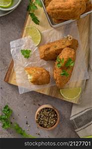 "Cod dumplings, or "bolinhos de bacalhau" and parsley leaves and lemons on wooden cutting board in a kitchen counter top."
