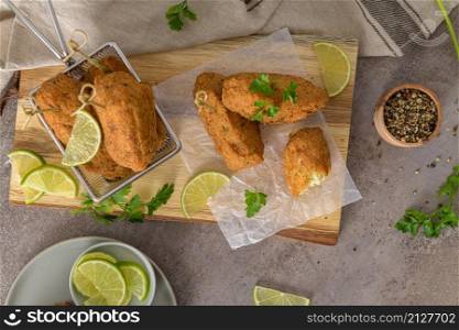 "Cod dumplings, or "bolinhos de bacalhau" and parsley leaves and lemons on wooden cutting board in a kitchen counter top."