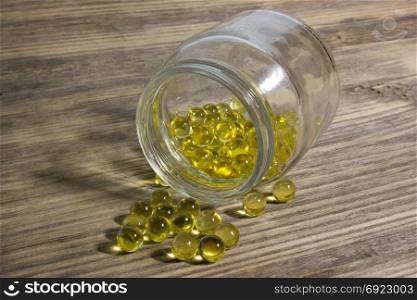 Cod fish oil gel capsules in glass jar on wooden background